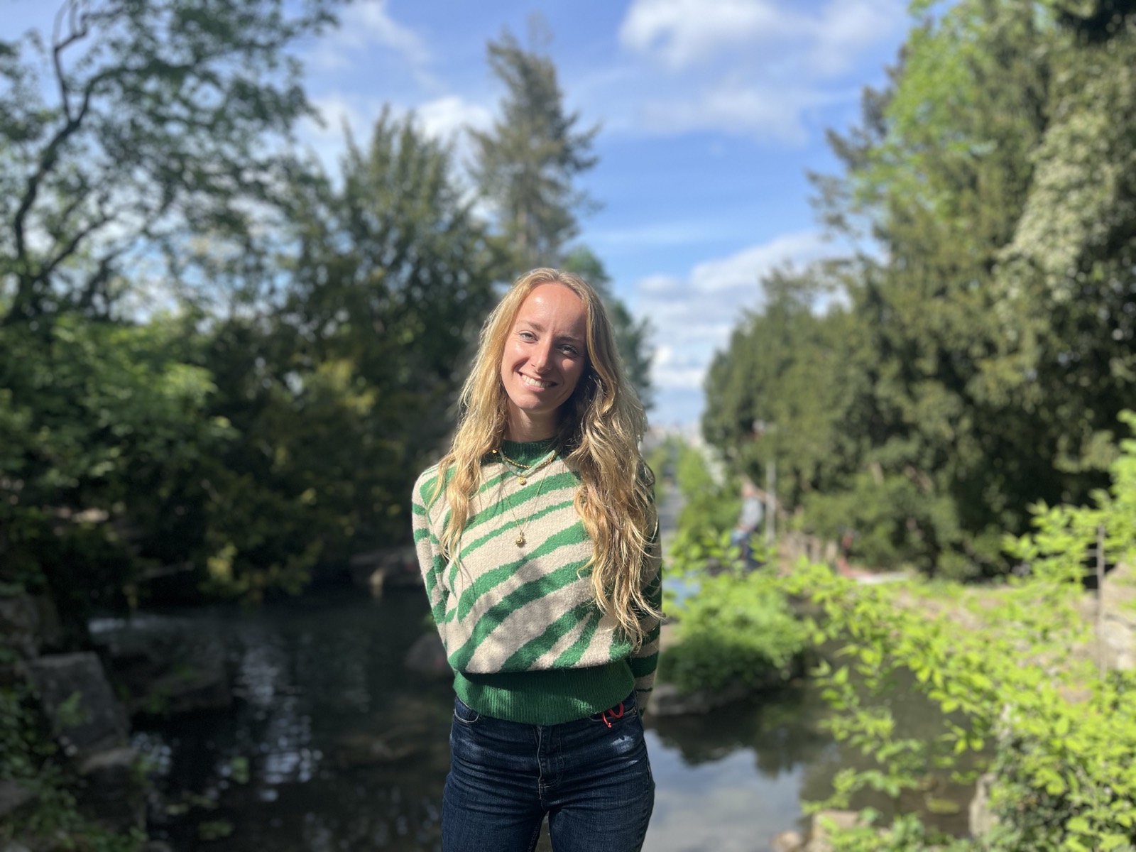 Sophia Müller, product designer, smiling outdoors by a tree-lined canal